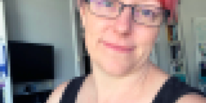 A picture of Karen that has been pixelated to look like a mosaic. Karen wears glasses, has pink and purple hair and is wearing a black top.