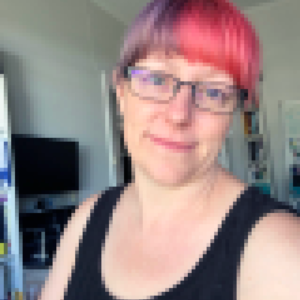 A picture of Karen that has been pixelated to look like a mosaic. Karen wears glasses, has pink and purple hair and is wearing a black top.