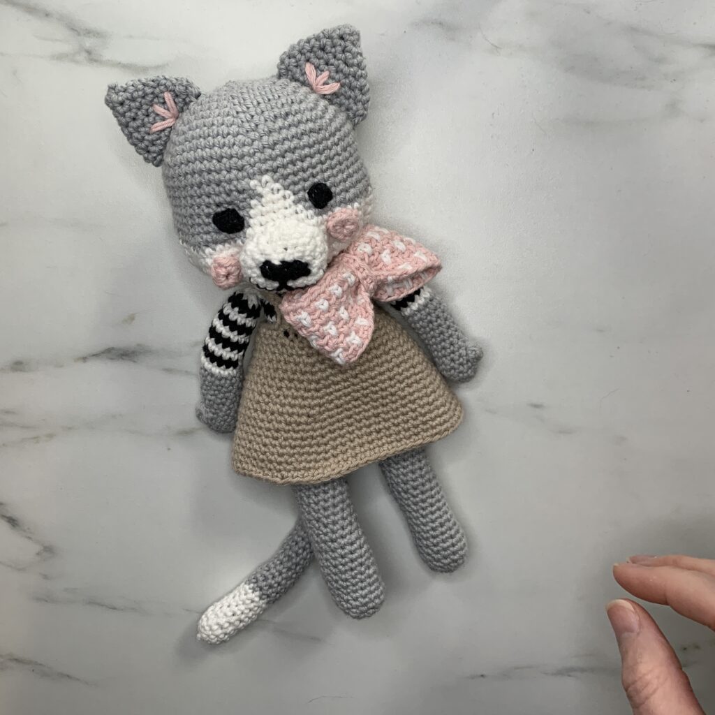 A crocheted soft toy of a cat wearing a dress and a bow tie.