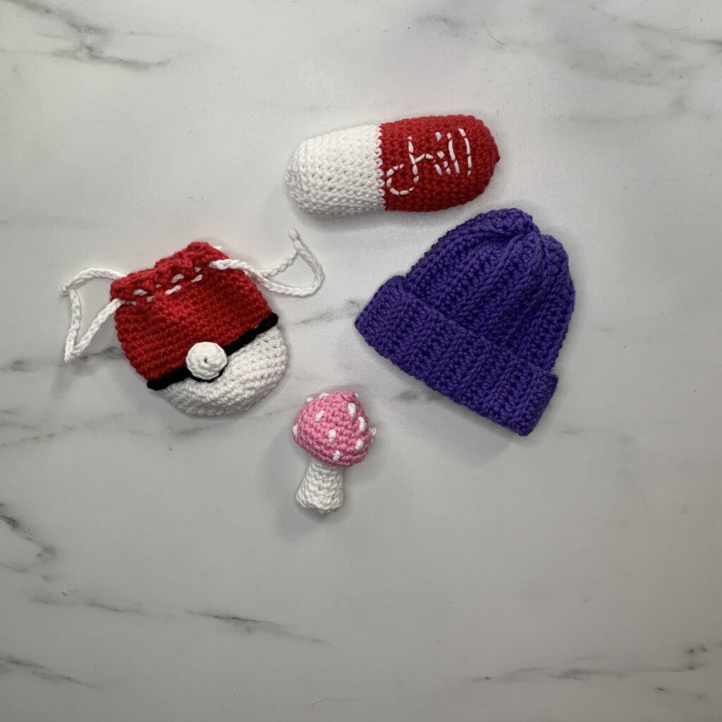 Assorted crochet pieces including a Pokemon drawstring bag, toy beanie and mushroom.